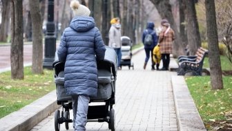 Mothers walking with baby prams on city street at autumn. Woman with stroller for twins in foreground